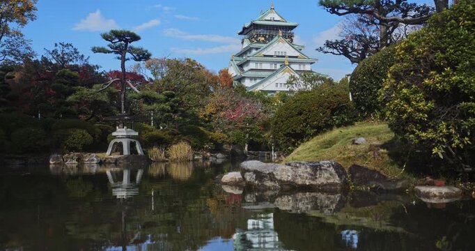 Shimmering little Japanese pond with majestic 16th century Matsumoto castle nearby - wide, low shot