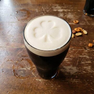 Glass of dark stout beer with shamrock shape in foam on wooden table, saint patrick day drink, ai generated.