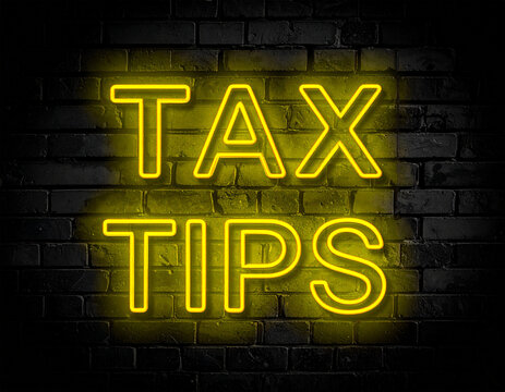 Leuchtende gelbe Neonschrift "Tax Tips" auf dunkler Backsteinmauer
