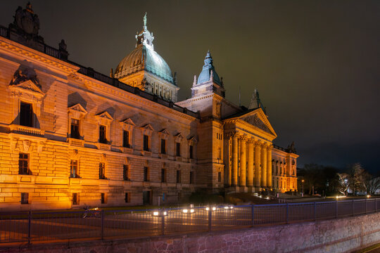View of warm light illuminating the Reich Court building beside the tranquil river, showcasing architectural grandeur in the night, Leipzig, Saxony, Germany.