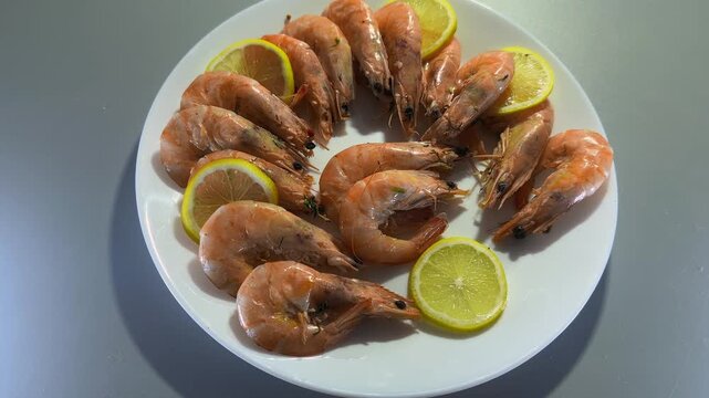 Boiled unshelled king prawns with lemon slices on white plate