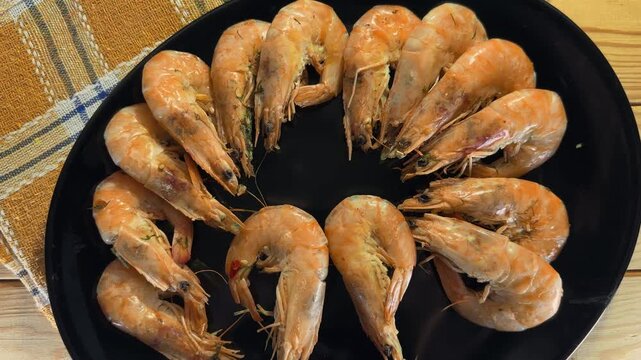 Boiled unshelled king prawns on black plate on rustic table