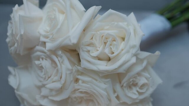 Close-up of a white rose bridal bouquet with stems wrapped in ribbon resting on a surface. Static shot.