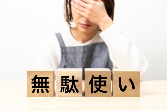 「無駄使い」と書かれたブロックとエプロン姿の女性