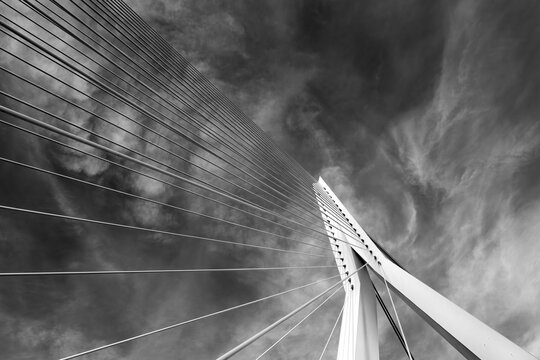 Pillar of a modern suspension bridge from a worm's-eye view in black and white with high contrast. Graphic architectural photo of the white-painted steel structure with sloping suspension cables. 