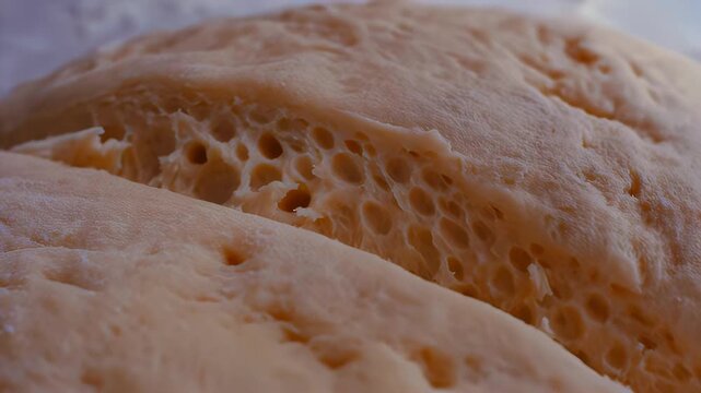 Close-up of dough being sliced with a sharp knife, revealing the airy texture and bubbles inside, set against a light countertop in a kitchen environment