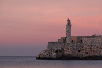 Castillo De Los Tres Reyes Del Morro lighthouse at sunset hour with orange, red and pink clouds in the background. Cuba, Havana waterfront. Sightseeing, historical landmarks, travel, tourism concept.