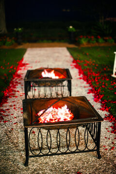 Fire pits along a walkway in a garden with scattered rose petals at night