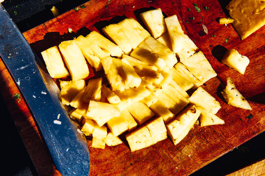 Slices of fresh pineapple next to a large knife on a wooden cutting surface