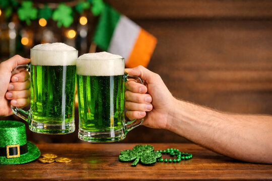 Friends clinking glasses of beer celebrating St Patrick's Day in pub. Holiday party concept with copy space.