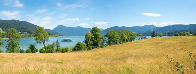 View across a summer meadow to Lake Tegernsee, passenger ship and Bavarian mountains