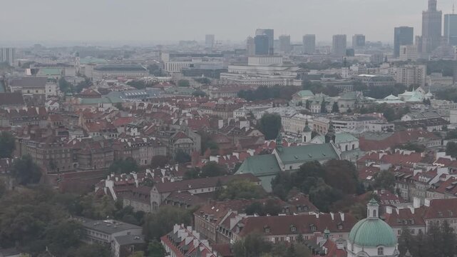 Aerial high-angle view over the red rooftops of Warsaw Old Town with the modern city skyline in the distance. Pan from right to left