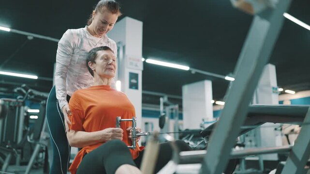 Personal trainer assisting senior woman on rowing machine