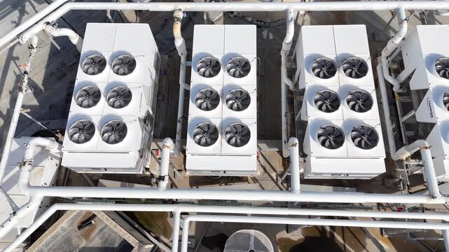 Aerial drone view of industrial rooftop cooling systems and ventilation units. Large HVAC equipment installed on commercial building roofs, including chillers, air conditioning compressors and mechani