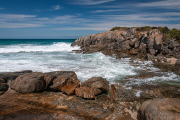 Rocky coastline in south west Australia with waves breaking against granite rocks, turquoise ocean water and dramatic sky. Rugged seaside scenery with clear water, stone formations and open horizon.