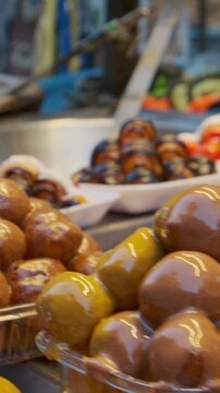 Assorted glazed zalabia or lugaimat dough balls arranged in rows at street vendor counter. Pastries are decorated with red, white, pink and chocolate icing, glossy glaze and decorative stripes