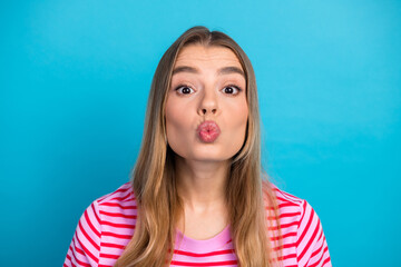 Playful young woman with blonde hair puckering lips in a pink striped t shirt against a bright blue...