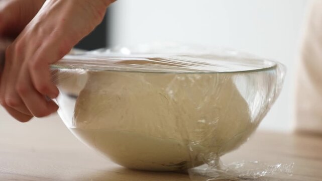 Hands covering dough with a stretch film