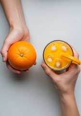 Hands holding a vibrant orange and a refreshing glass of juice with ice