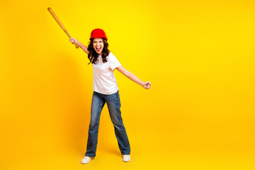 Young woman construction worker in red helmet cheerfully swings a bat against a bright yellow background