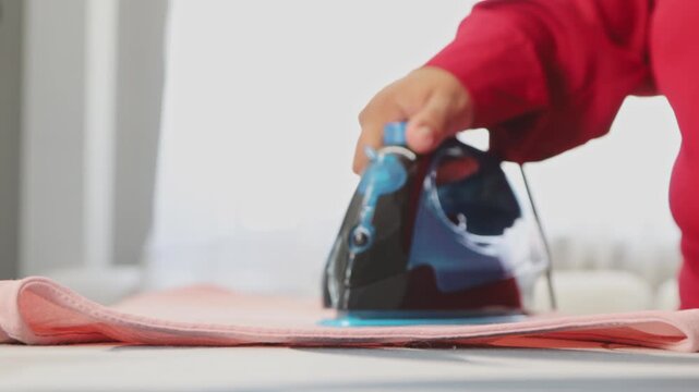 A woman gently irons a soft pink blouse on an ironing board at home, focusing on maintaining the delicate fabric smooth and neat, preparing it for work, school, or an outing.