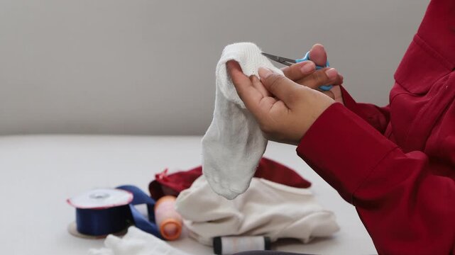 A woman carefully cuts loose threads from a child&rsquo;s garment, performing simple home clothing care with attention and precision.