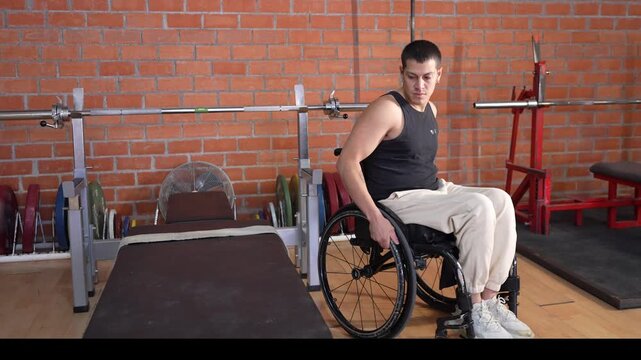 Determined disabled athlete in a wheelchair transferring himself onto a weightlifting bench, preparing for an intense training session in a gym