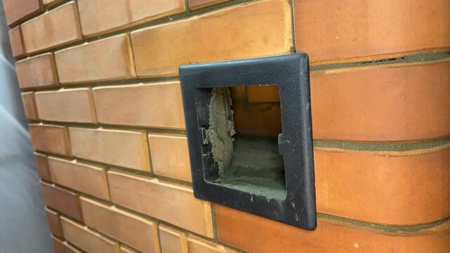 Man demonstrating a cleanout door on a heating stove. Close-up. New brick heating stove. Construction of a wood-burning stove.