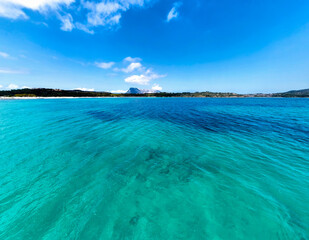 Low angle view of turquoise water at Lu Impostu beach with Tavolara island and cloudy blue sky