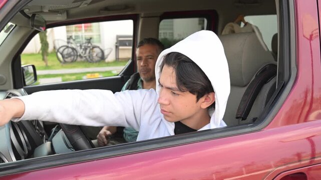 Teenage boy adjusting the car side mirror during a driving lesson.
