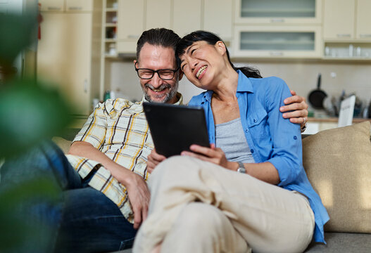 Portrait of a lovely young couple using a tablet computer together and having fun sitting on sofa at home