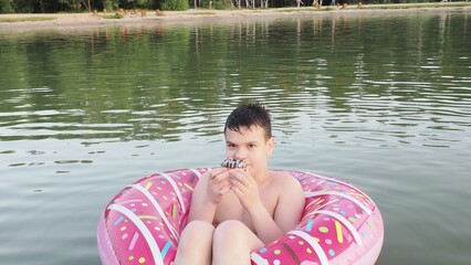Fototapeta premium A teenager boy swims in a lake. A child jumps into a lake outdoors. Happy parents and a child enjoy their summer vacation and play in the river. Enjoying their vacation, eating a snack.