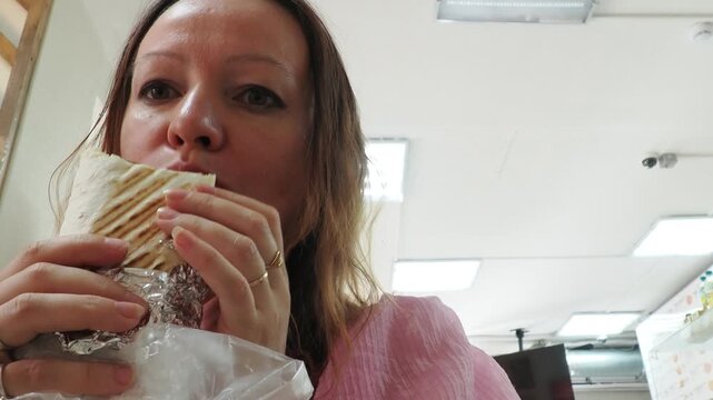 a woman sits and eats in a cafe. Female hand holding fresh tortilla wrapped. Gourmet concept. tasty chicken Doner kebab or shawarma. Vegetarian Tortilla wrap with falafel and salad, tacos. Junk food.