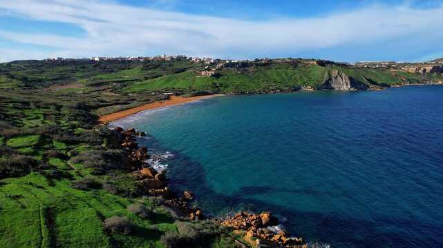 Aerial drone view of the most beautiful Malta beach in Gozo, vibrant red sand Ramla beach with crystal clear blue water and mesmerizing waves with lush green vegetation around it and the famous Mixta 