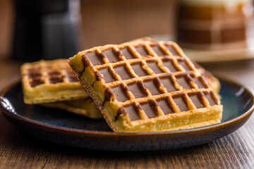 Sweet waffles with chocolate on plate on wooden table.