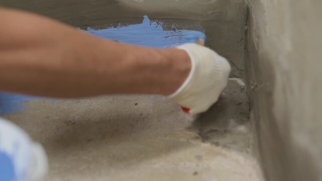 Worker applying blue waterproofing liquid to concrete floor