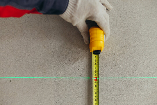 Hand Holding Tape Measure Vertically Along Laser Line On Wall. Height Measurement In Construction Setting.