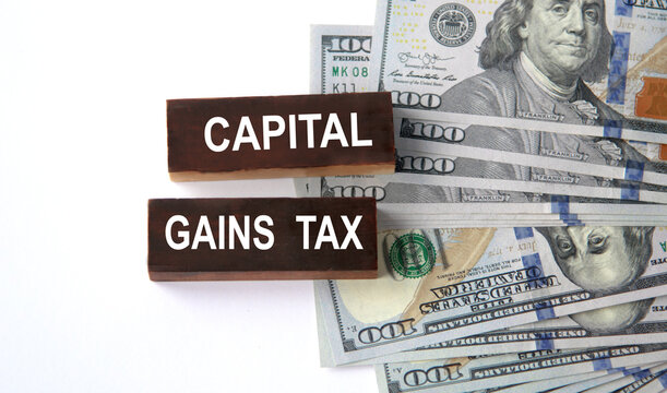 CAPITAL GAINS TAX - inscriptions on wooden blocks on a white background with images of banknotes.