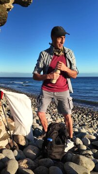 Ecological activist taking a break from cleaning the beach, drinking fresh water from his reusable bottle to stay hydrated while enjoying the sunny day and the beautiful sea view