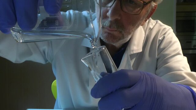 Male scientist pouring liquid in a laboratory beaker