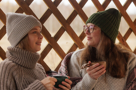 Two friends share warm drinks and laughter on a cozy winter afternoon by the window