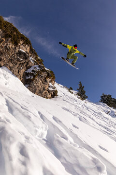 Snowboarder jumps mid-air off snowy mountain cliff