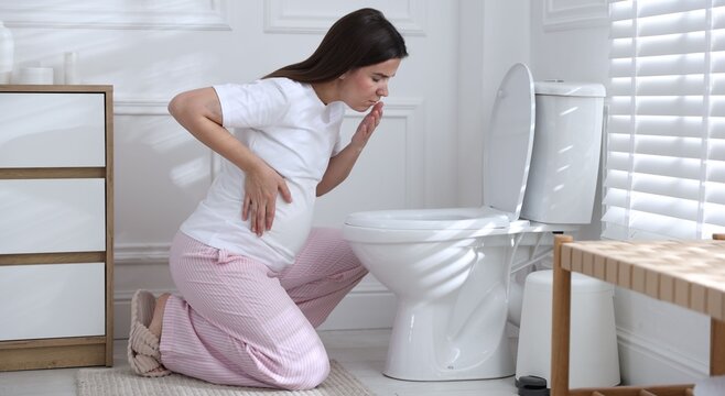 Pregnant woman suffering from nausea over toilet bowl in bathroom. Toxicosis during pregnancy