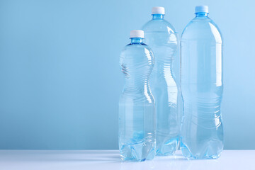 Water bottles of different sizes on white table against light blue background. Space for text