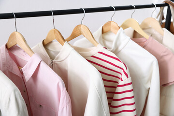 Plakat Different stylish clothes hanging on rack against light grey background, closeup