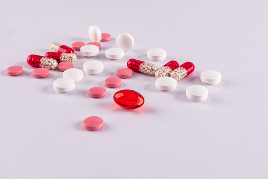 Various pills and capsules scattered on white surface