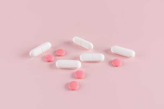 Various pills and capsules on a pink background