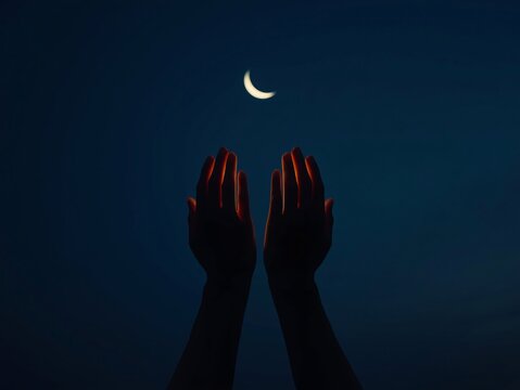 Silhouetted hands raised in prayer beneath a glowing crescent moon in the night sky.