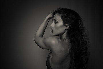 Fototapeta premium Elegant sexy woman with long curly hair posing in elegant dress with nude back and shoulder. Slim body, health skin. Profile face view. Art black and white color portrait. Vogue closeup style.