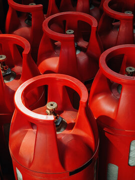 Red composite gas tanks with brass valves. Close-up of vibrant red industrial LPG gas cylinders, the space filled with beams of light.